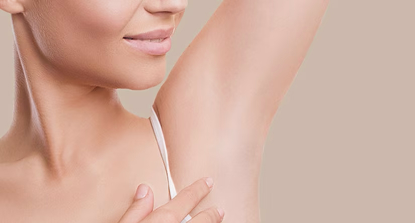 Close-up van de gladde, verzorgde oksel van een vrouw met een opgestoken arm. Een deel van haar gezicht is zichtbaar en ze lacht zachtjes.
