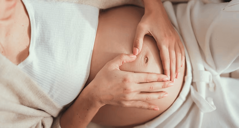 Close-up van een zwangere buik, waarop de persoon met de handen een hartvorm maakt rond de navel.