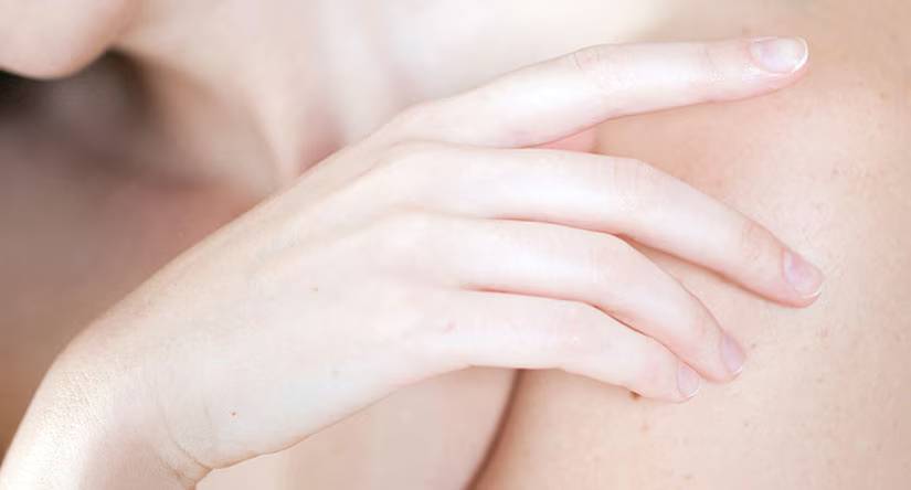 Close-up van een hand met een lichte huidskleur die teder op de eigen schouder ligt.