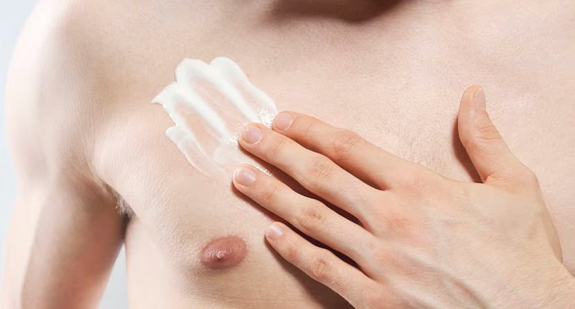 Close-up van een man met een lichte huidskleur die met zijn hand een dikke, witte crème uitsmeert op zijn borst.