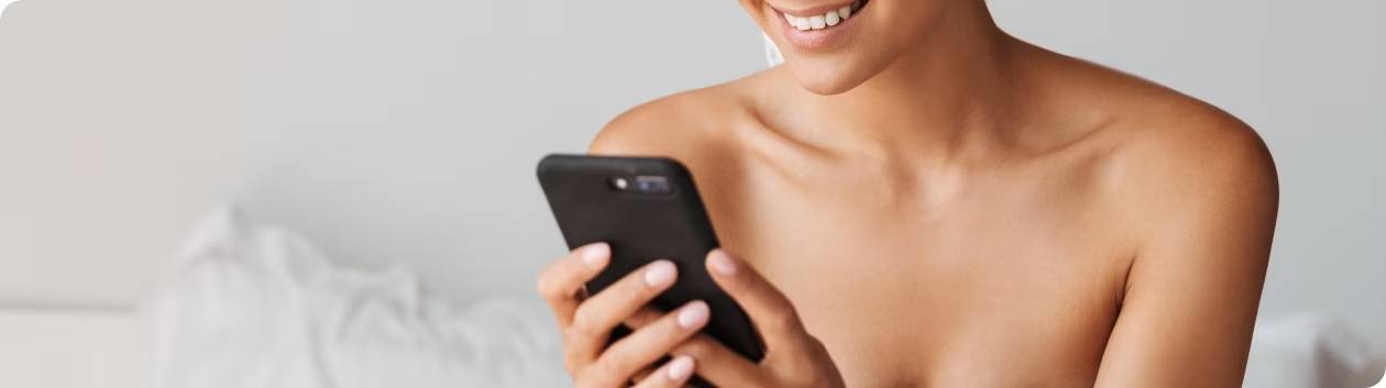 Vrouw met perfecte huid glimlacht terwijl ze naar haar mobiel kijkt